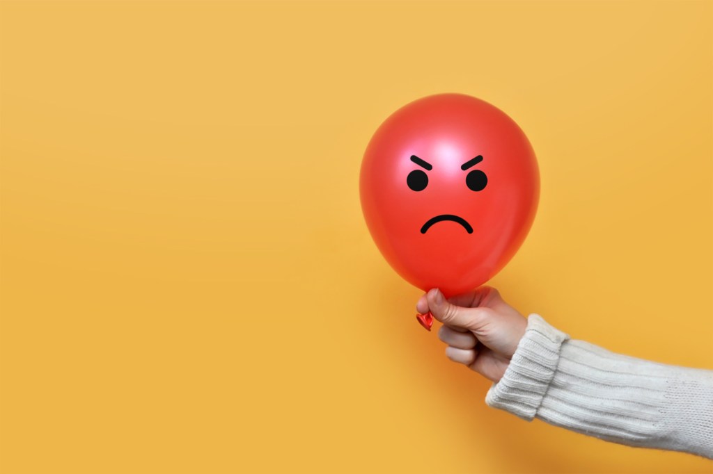 Person holding a red balloon with an angry face drawn on the balloon.