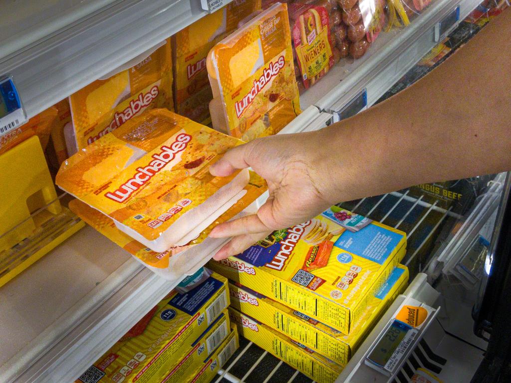 Shopper's hand selecting two Oscar Meyer Lunchable packages from a refrigerator in a grocery store