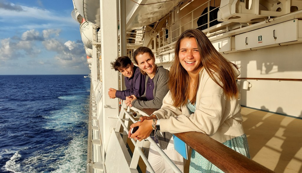 A happy family standing on the deck of a Royal Caribbean cruise ship gazing out at the ocean