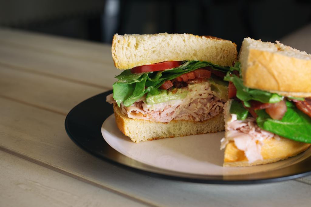 Turkey club sandwich with bacon, avocado and tomato on sourdough bread, cut into two halves