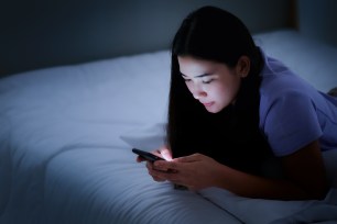Woman looks at her phone in bed.