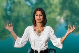 Yoga meditation retreat. Woman sitting in lotus position with fingers in Chin Mudra and meditating by the lake