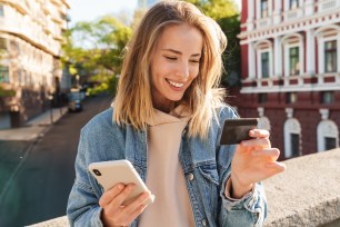 A woman happily uses her phone and credit card to purchase online items.