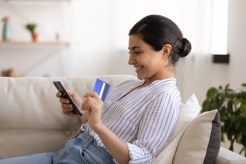 A woman uses her phone and credit card to shop online.