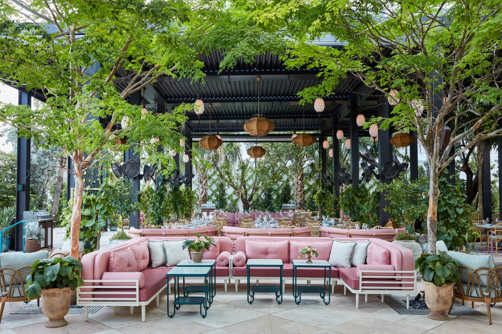 Exterior image of Casadonna restaurant, featuring a pink couch under trees and hanging lights.