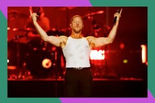 Imagine Dragons frontman Dan Reynolds triumphantly raises his arms while addressing the crowd.