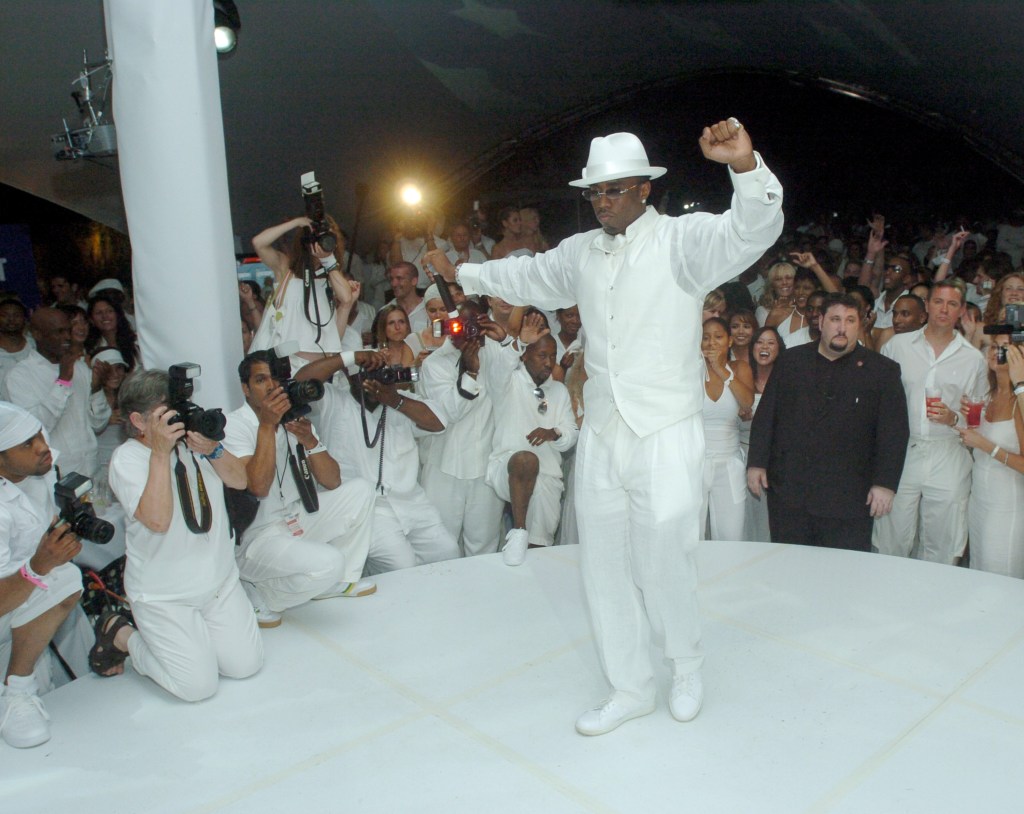 Sean 'P. Diddy' Combs in a white outfit, standing on a stage at the PS2 Estate, during the 6th Annual P. Diddy White Party in Bridgehampton, New York, surrounded by a crowd.