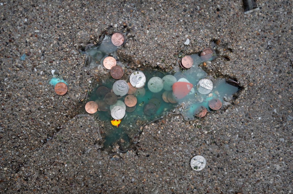 Coins are left behind by visitors at an impression in a sidewalk known as the Chicago Rat Hole.
