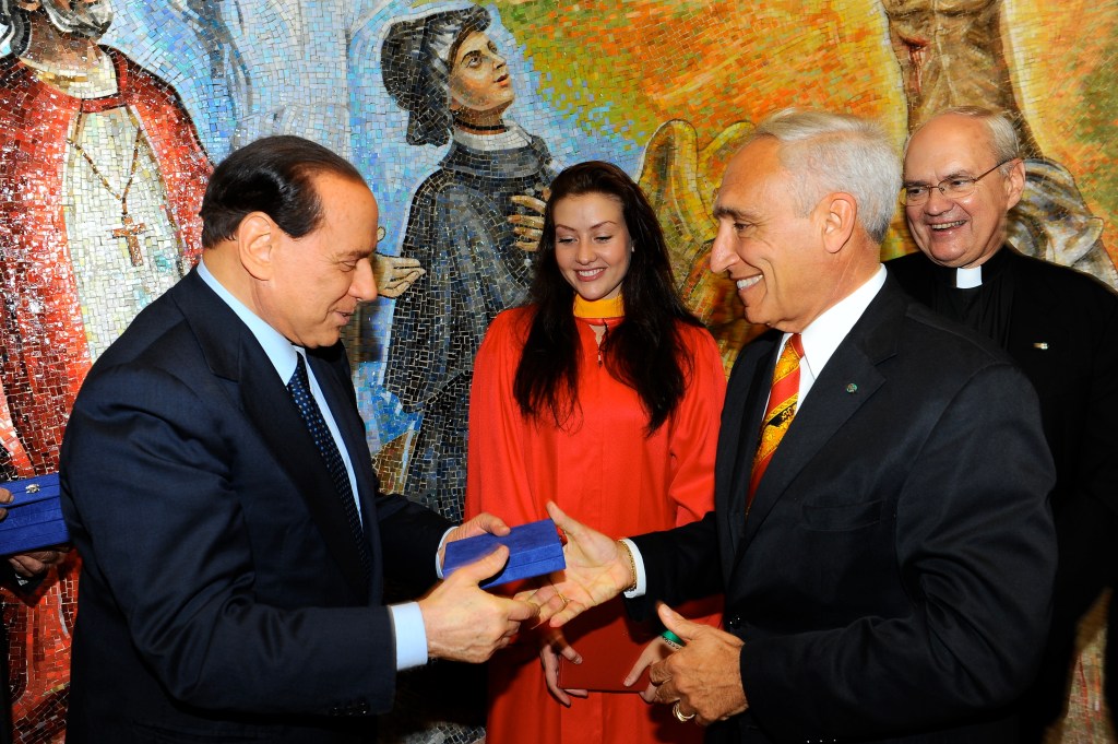 Silvio Berlusconi handing a blue box with an Italian paperweight to a smiling Joe Sciame at Eleonora's graduation reception at St. John's chapel.