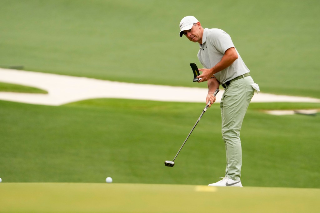 Rory McIlroy hits a one-handed put while holding a yardage book during a practice round at Augusta National. 