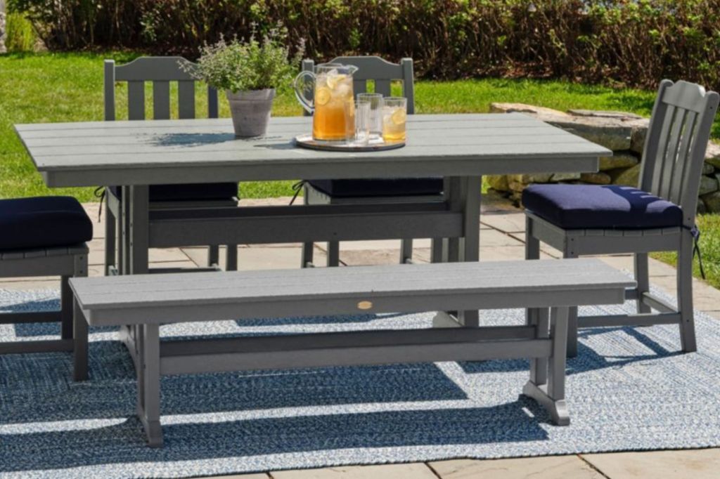 An outdoor dining table and bench with drinks and a plant on the table top.