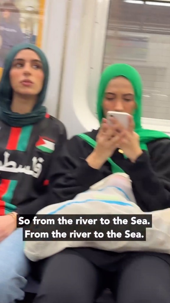 Two women sitting on a subway train looking at a phone during an Anti-Israel protest in New York City