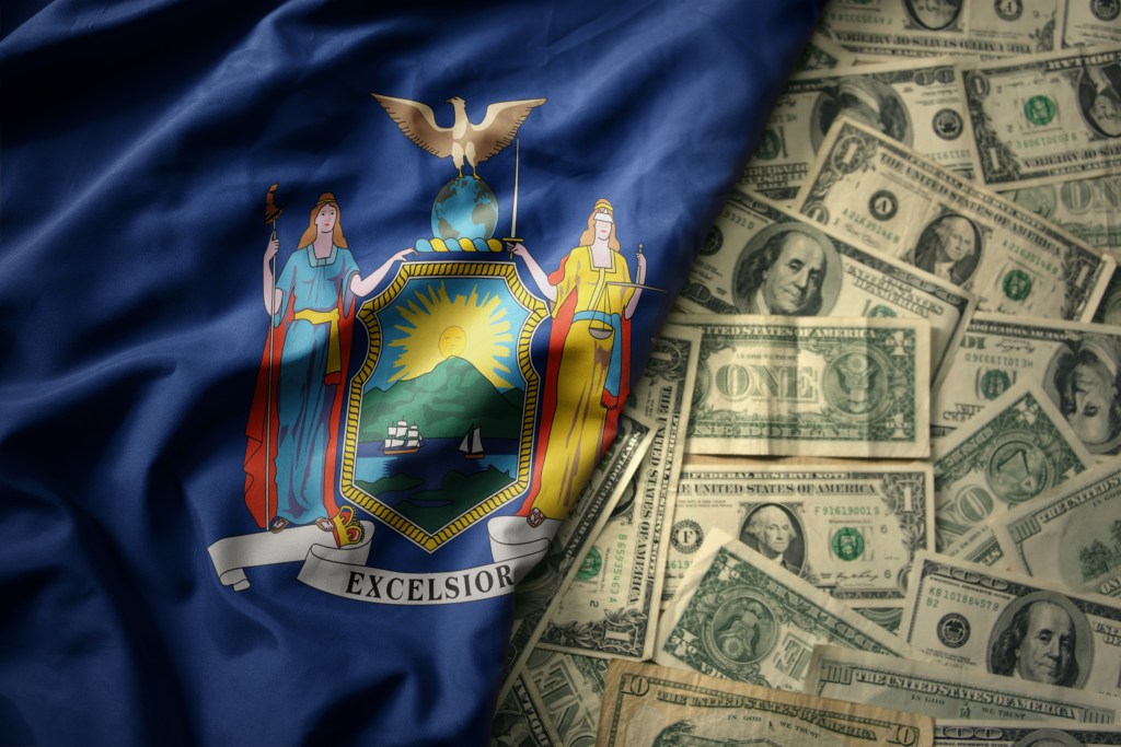 Stock image: New York State flag next to a pile of one-dollar bills