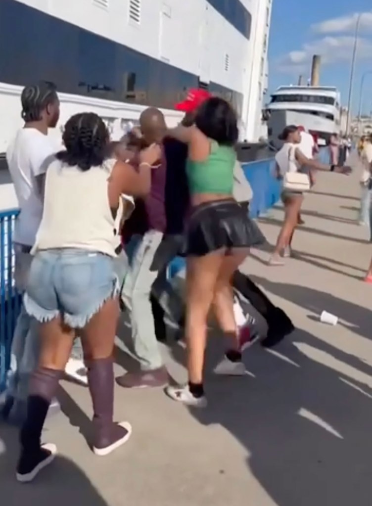 Several men and women can be seen pushing and shoving each other on the pier right next to the massive yacht. 