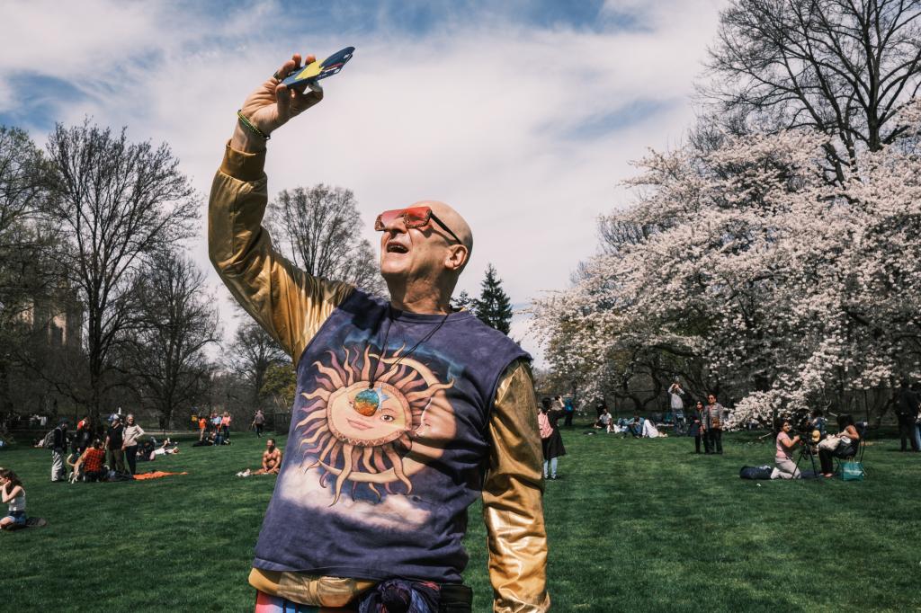 A man taking a picture of the eclipse with his phone in Central Park.