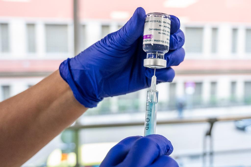 A latex gloved hand drawing medicine into a syringe from a vial.