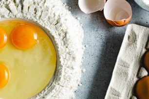 Eggs in a heap of flour surrounded by other ingredients.