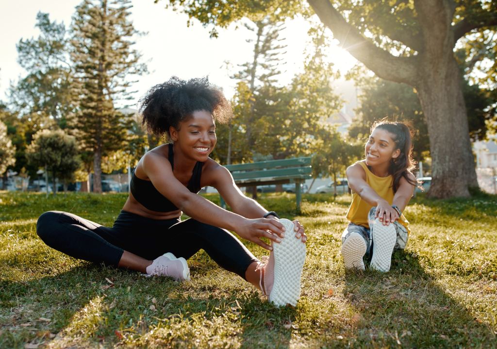 A group of diverse female friends warming up by doing stretching exercises in the park