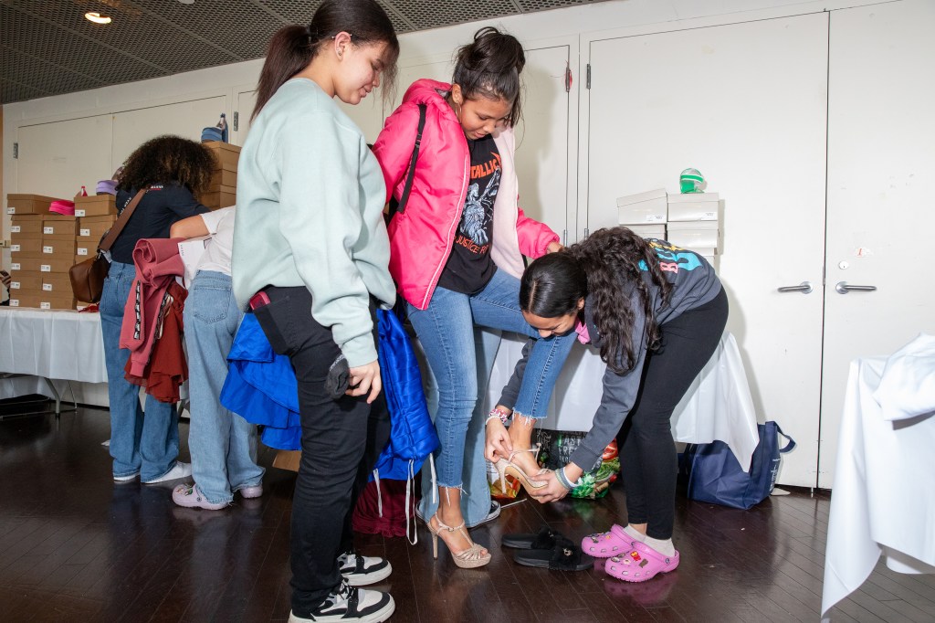 Friends helping each other try on shoes at a prom clothing giveaway event by the non-profit Operation Prom at the Dominican Community Center