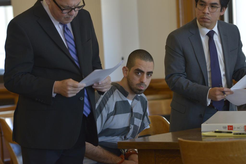 Hadi Matar, handcuffed in court in a striped shirt, surrounded by lawyers