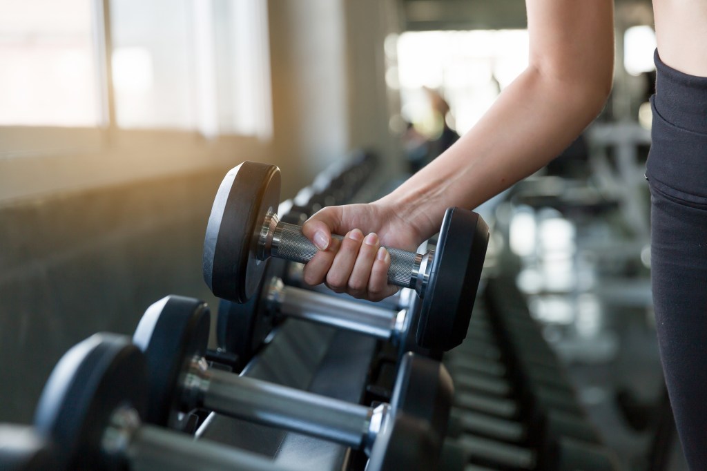 Hand of athlete woman holding dumbbell from the rack in the gym.