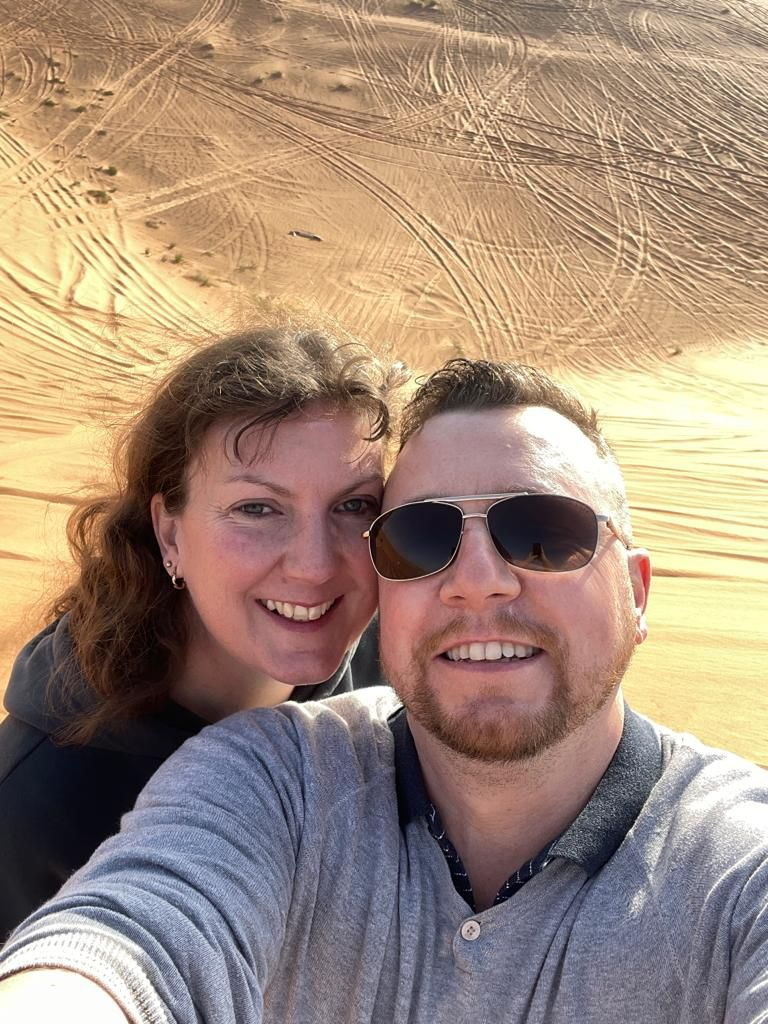 A man and woman, Charlotte Robertson and Glen, taking a selfie in the desert, happily married after meeting at a Tesco supermarket.