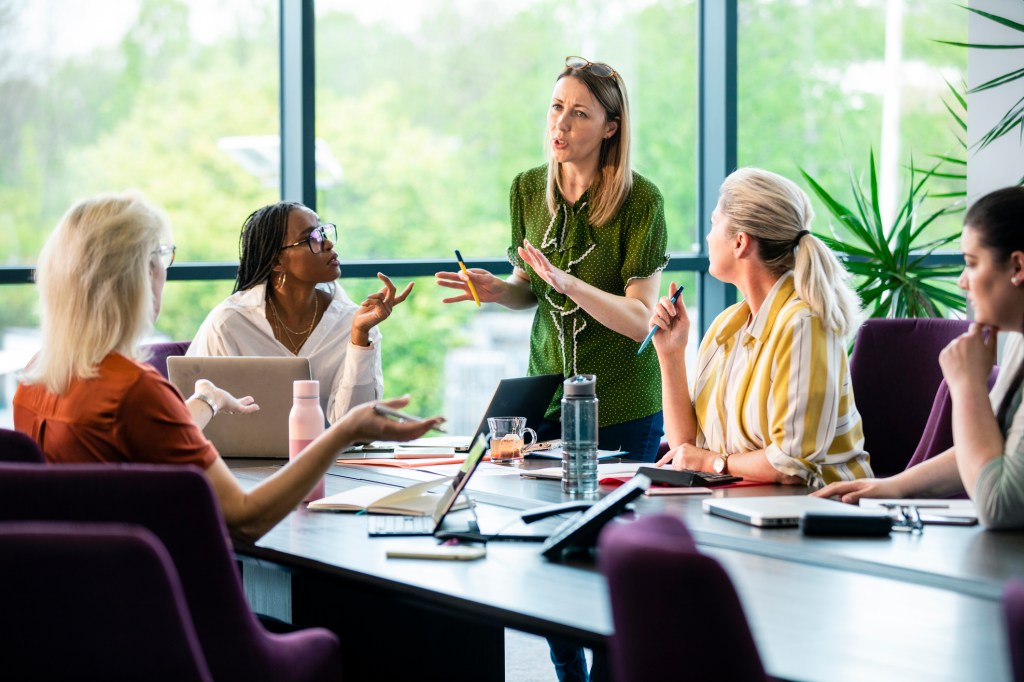 Wide-angle view of a board room with a group of women discussing ideas and working collaboratively on business opportunities