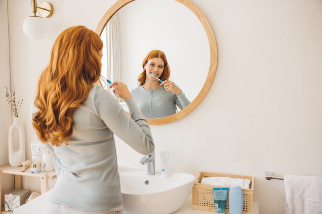 Young woman at bathroom brushing teeth with  toothpaste.