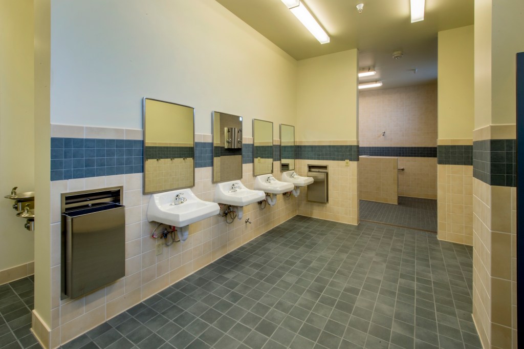 Men's restroom in a small secondary school, featuring sinks, mirrors, and an attached shower room.