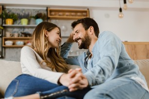 A happy couple sitting on a couch at home, talking and holding hands