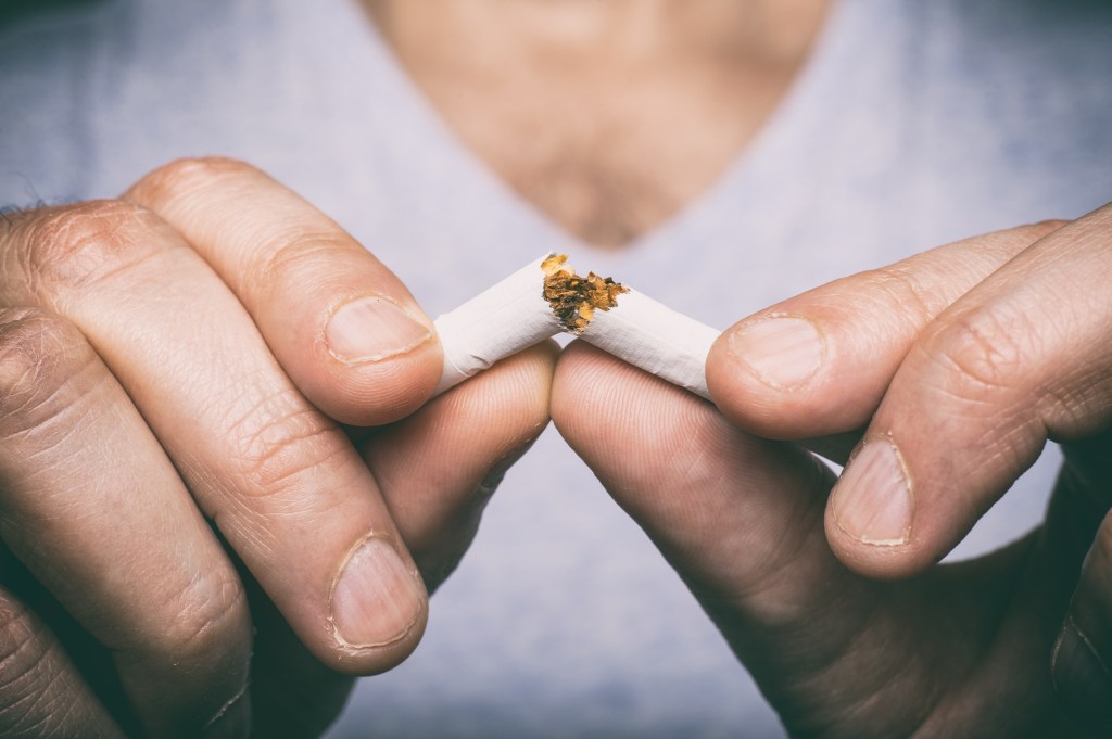 Close-up of a person's fingers breaking a cigarette in half.