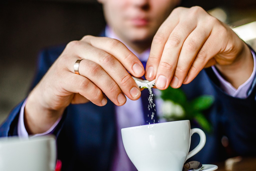 Closeup on someone's hands pouring sugar into coffee cup