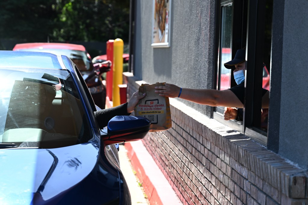 A McDonald's drive-thru in Belmont, California with a person wearing a mask and holding a bag of food