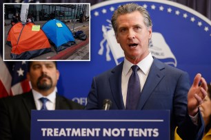 Gavin Newsom speaking at a podium at a Veterans Day Parade in Miami Beach, Florida, with Girl Scouts and Brownies holding American flags in the background