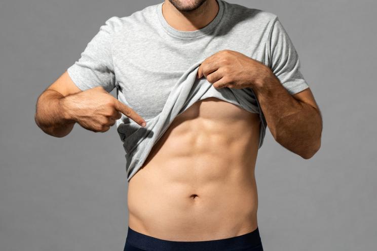 Muscular male model lifting up his t-shirt to show abs on a gray isolated studio background