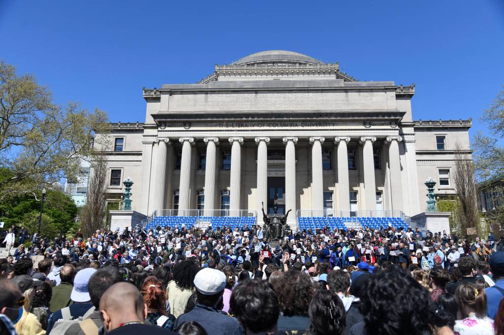 A large group of people stand facing the steps of the library on Columbia University's campus.