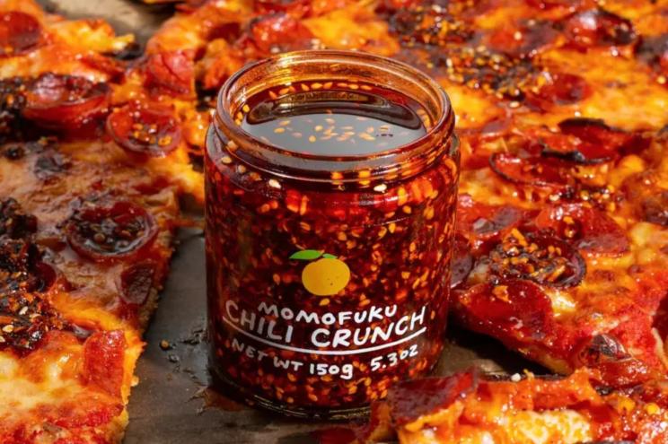 Open jar of Momofuku Chili Crunch surrounded by pizza with the Chili Crunch on it.