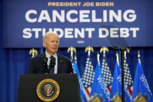 President Joe Biden standing at a podium with microphones and flags behind him, announcing a new student loan forgiveness program at Madison Area Technical College, Wisconsin