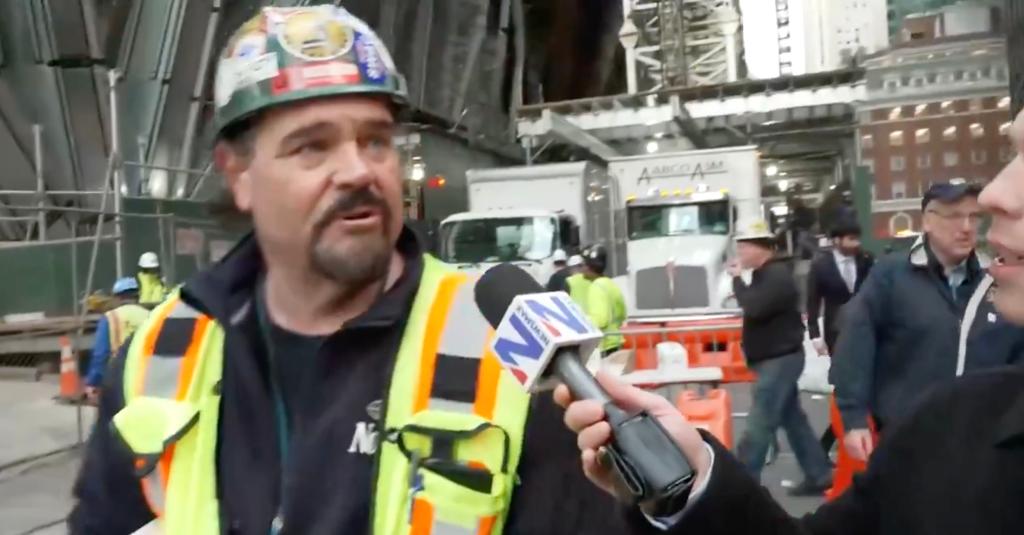 Construction worker in hard hat and vest speaks to Newsmax reporter.
