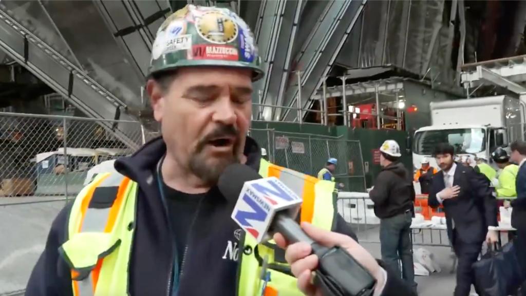 Construction worker in hard hat and vest speaks to Newsmax reporter.