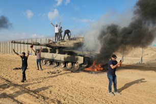 Palestinians celebrate by a destroyed Israeli tank at the Gaza Strip fence east of Khan Younis Saturday, Oct. 7, 2023.