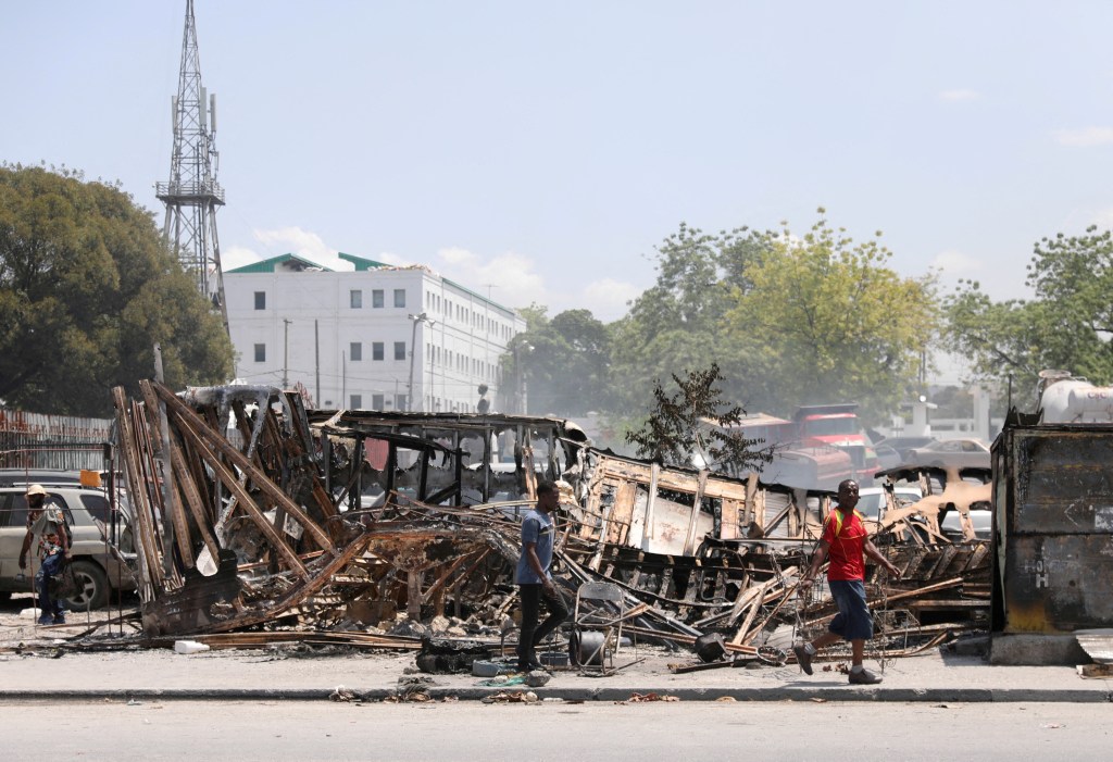 People walking past burnt vehicles near the presidential palace in Port-au-Prince, Haiti amidst increasing gang violence