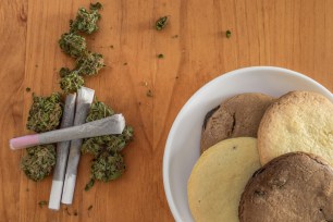 Pile of marijuana buds with rolled joints and a dish with homemade cookies of marijuana on wooden table. Breakfast of weed and cookies.