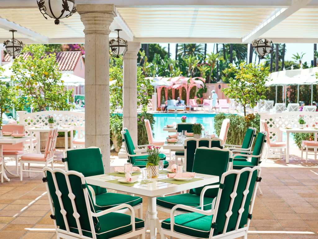 A table and chairs set outside at the renovated Beverly Hills Hotel, with a pool in the background