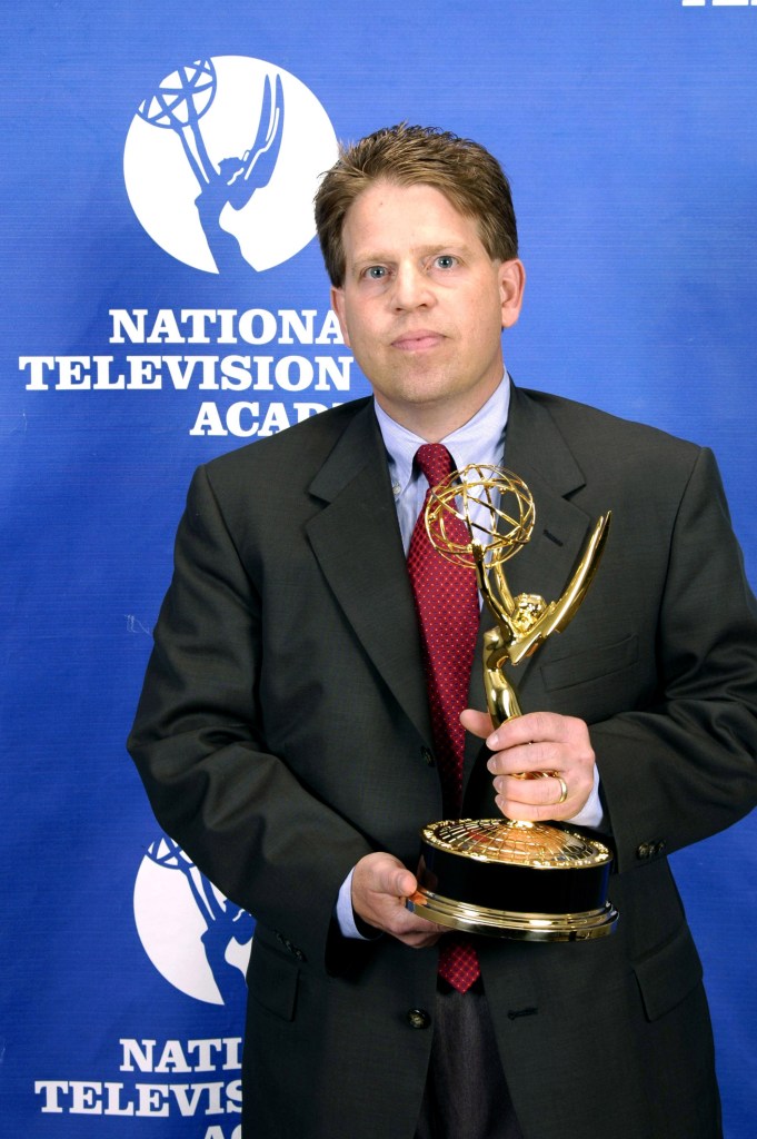 Norby Williamson in a suit holding a trophy at the 26th Annual Sports Emmy Awards in New York City.