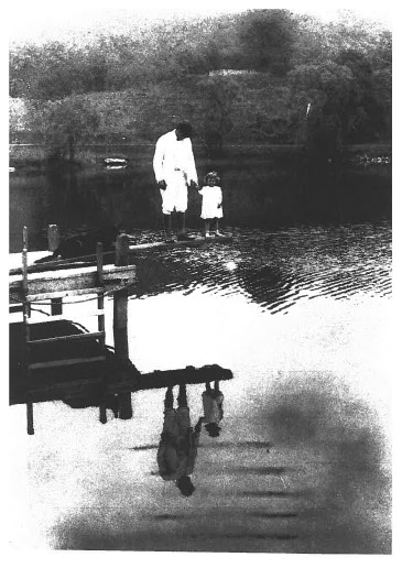 An archival image of a man and a girl down at the property's lake.