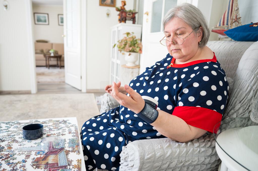 Senior woman measuring her blood pressure with a medical electronic tonometer while sitting in a brightly lit room at home