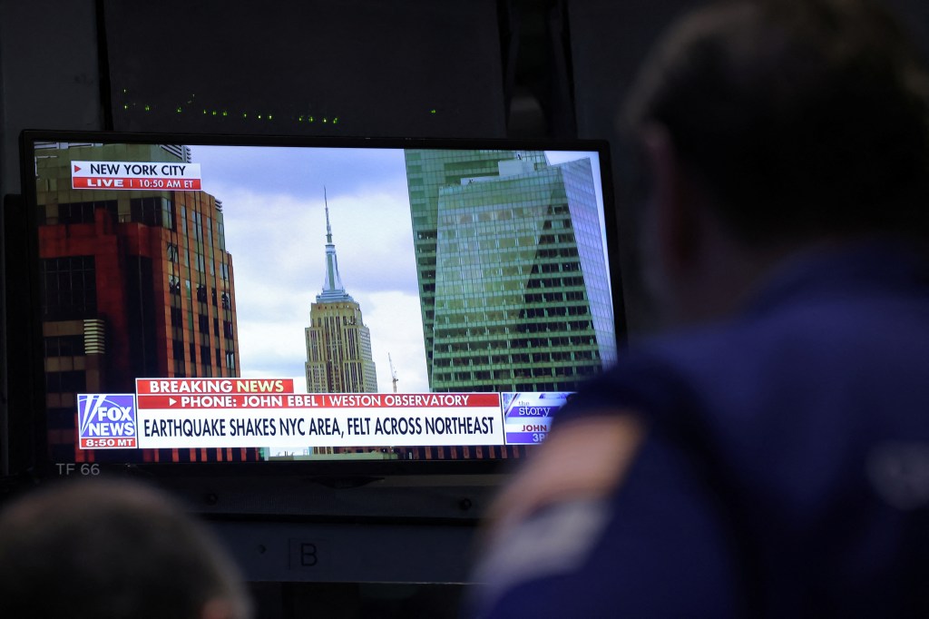 Man observing the news alert about a magnitude 4.8 earthquake in New York City on a screen at the New York Stock Exchange.