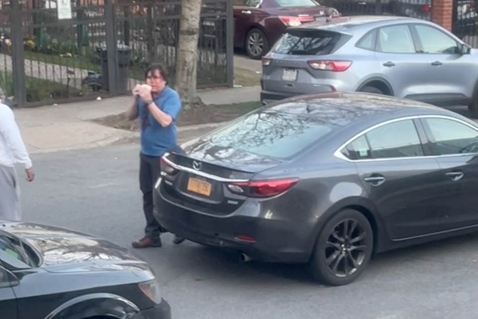 the driver, covered in blood dripping from the top of his head, standing near his car after the assault.