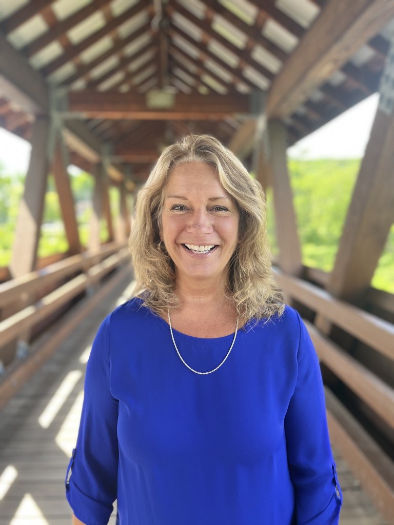 State Senator Carrie Gendreau smiling at camera with LGBTQ murals on main street buildings in the background in Littleton, NH